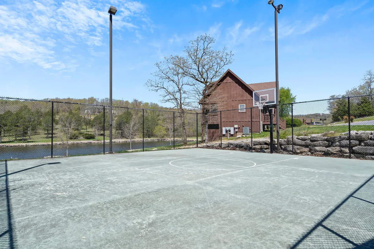 A basketball court nestled in a scenic outdoor setting, with a view of the lake, lush landscapes, and a wooden house nearby. The environment invites energetic play as well as peaceful relaxation by the water.