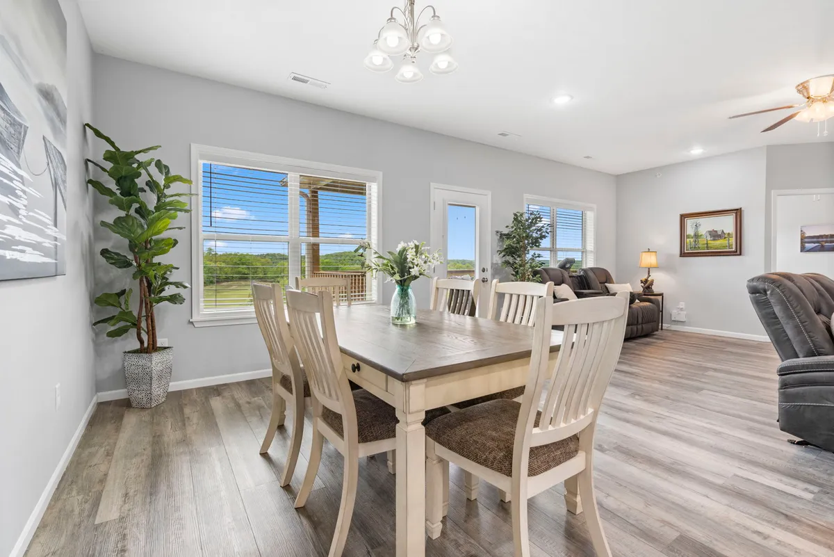 This inviting interior showcases a sunlit dining area with a stylish modern table, a vibrant floral centerpiece, and expansive windows offering picturesque views. The setting exudes warmth and cheer, perfect for family meals, festive celebrations, or relaxing brunches with friends.