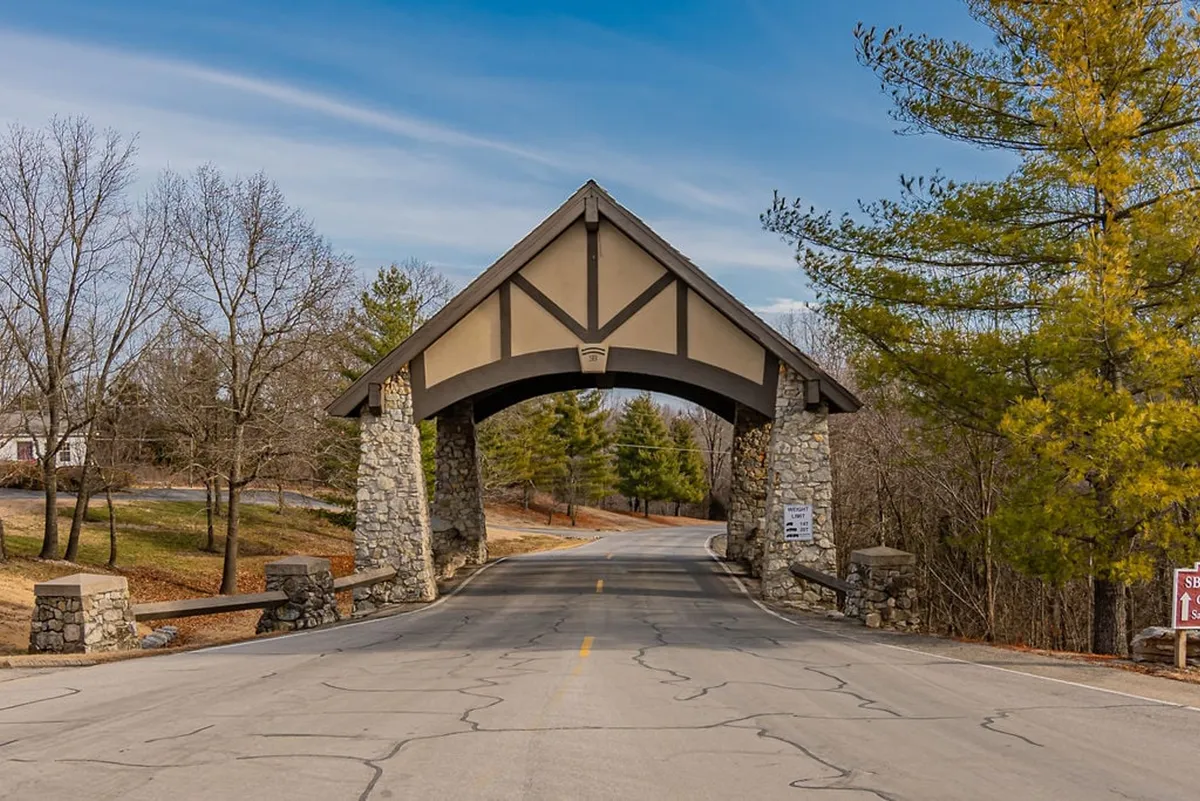 A welcoming stone archway marks the entry point to a tree-lined roadway and the beginning of nature trails, evoking a sense of arrival and adventure in a serene environment.