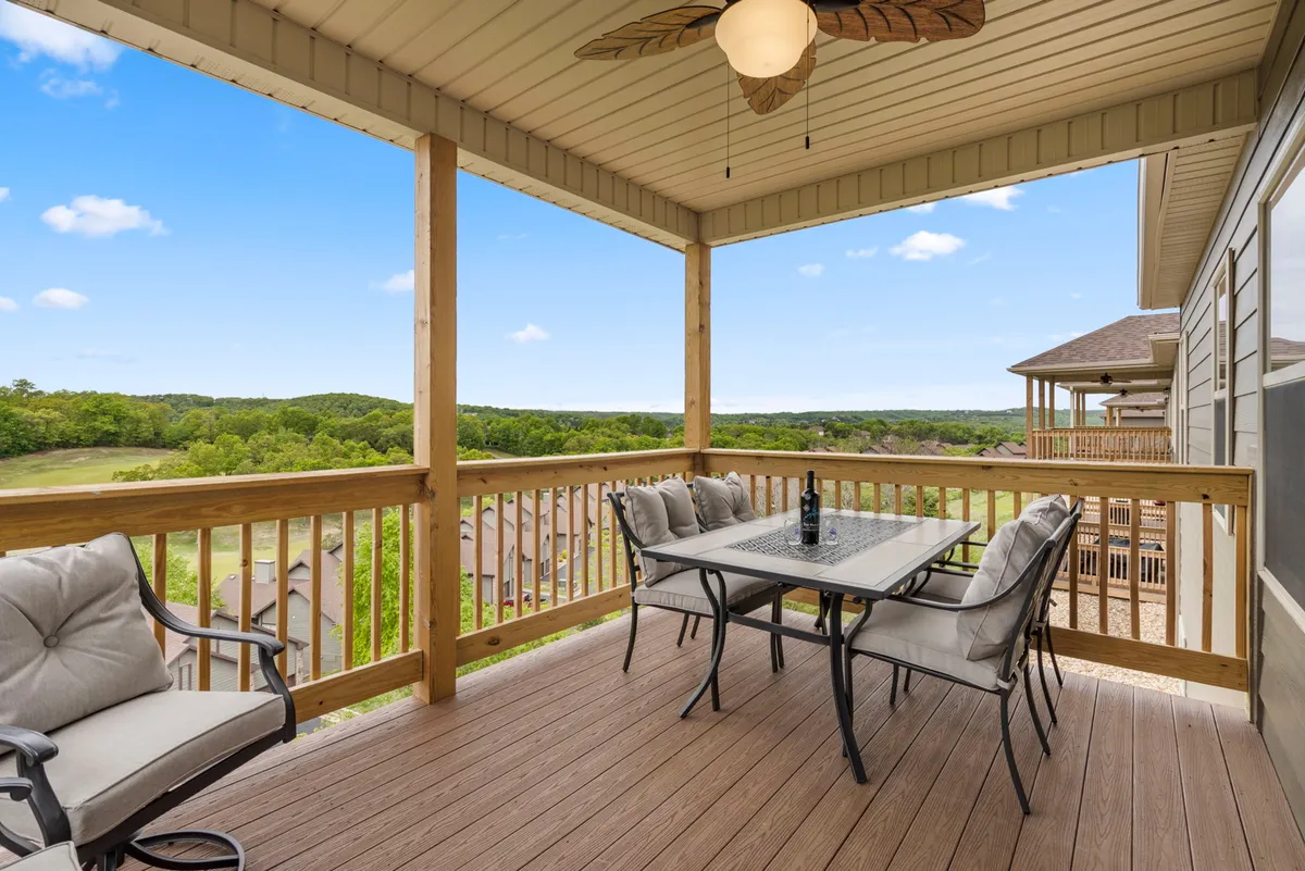 An inviting outdoor deck features a sturdy dining table with comfortable seating, all set against a stunning backdrop of rolling green Ozark hills. The scene suggests relaxation and socializing, with the deck acting as a seamless transition between the comfort of the home and the beauty of nature.