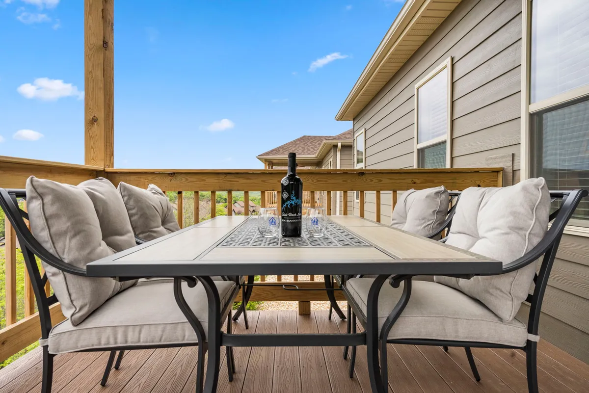 A cozy outdoor table setting complete with a wine bottle, glasses, and cushioned seats, all positioned to take advantage of a breathtaking view. The scene is bathed in warm light, suggesting peaceful afternoons or celebratory evenings spent outdoors.