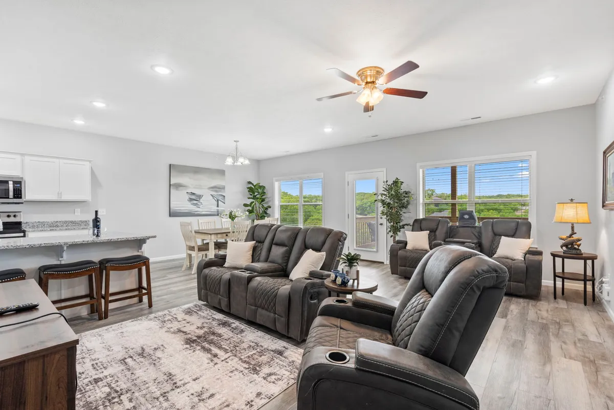 This image presents a welcoming open-concept interior combining a plush reclining sofa, a spacious dining table, large sunlit windows, and tasteful artwork. The layout makes it easy to move between relaxing, socializing, and dining, embodying a modern and communal atmosphere.