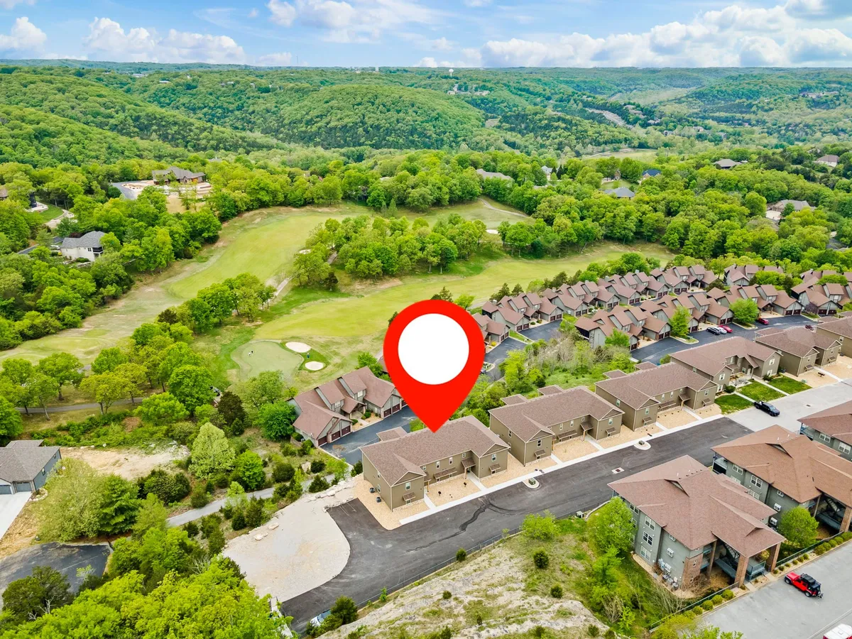 Rows of townhouses border the edge of a manicured golf course, with rolling green hills stretching into the background. The serene setting is bathed in soft light, evoking a sense of community and tranquility.