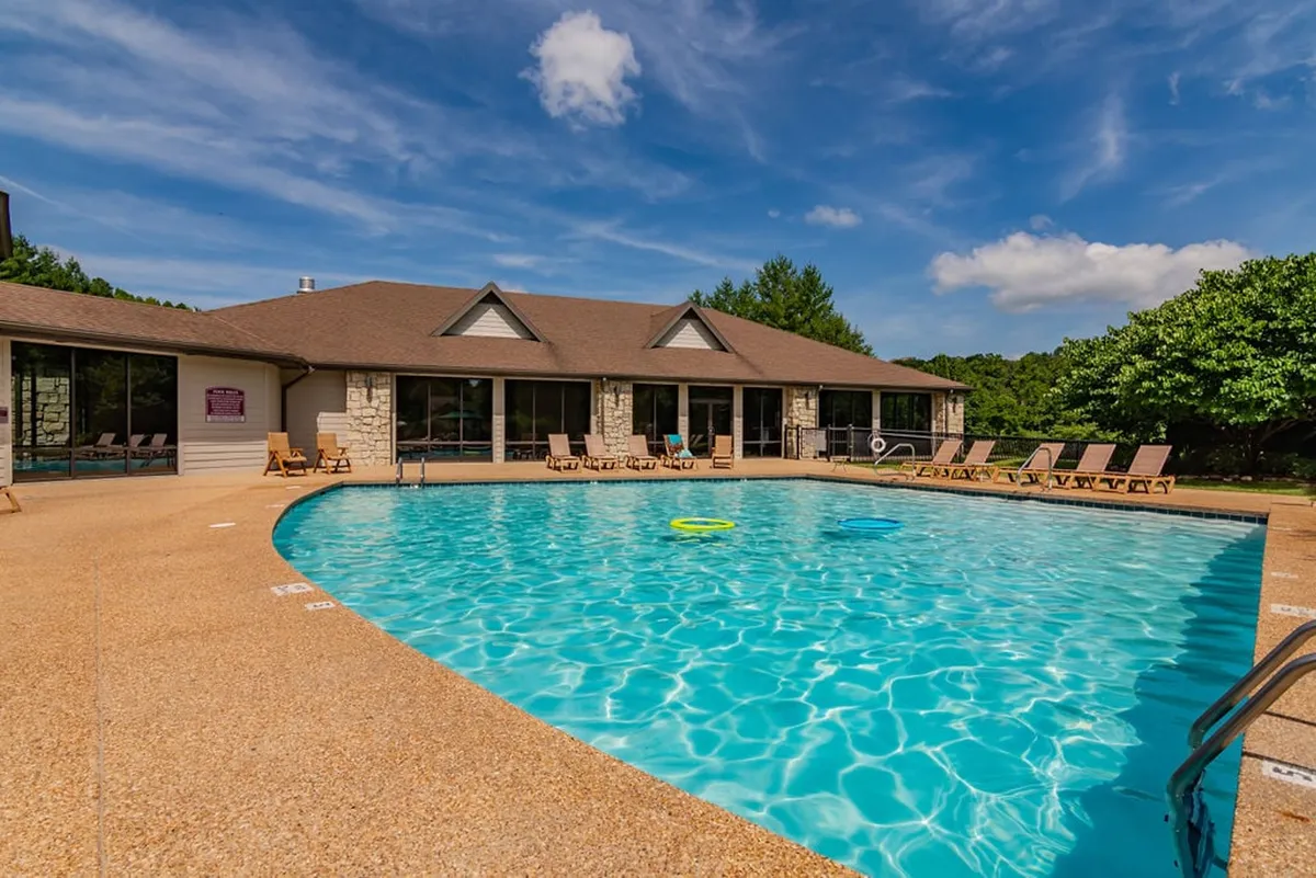 A beautiful swimming pool scene with lounge chairs arranged for sunbathing, the building’s facade in the background, and lush landscaped greenery. The inviting water and leisure setup captures the essence of seasonal relaxation and social gatherings.